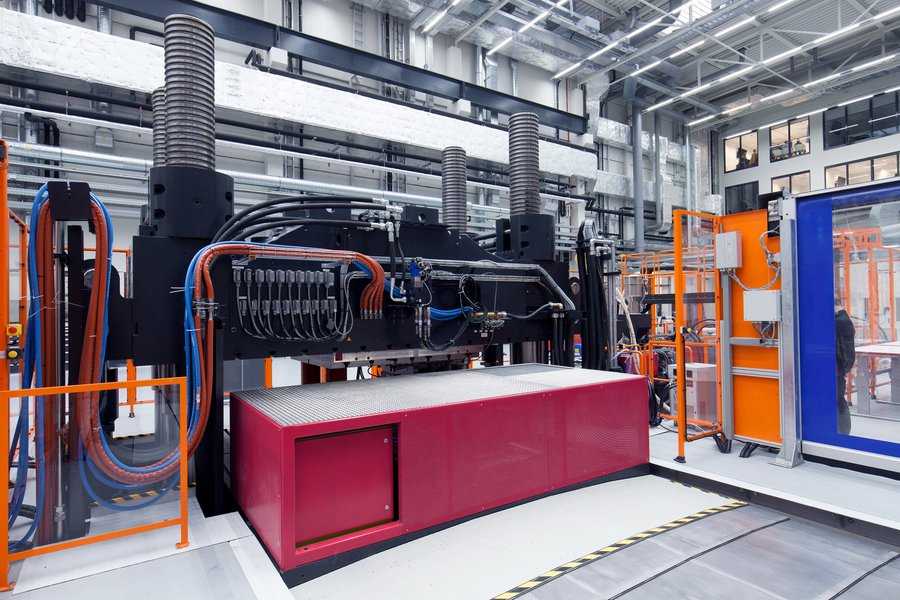 Eine moderne Industriemaschine mit zahlreichen angeschlossenen Kabeln und Rohren, die sich in einer geräumigen Fabrikumgebung mit heller Beleuchtung befindet.