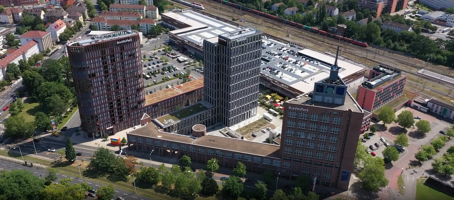Luftaufnahme einer Stadt mit Gebäuden des Brawo Parks und einem vorbeifahrenden Zug.