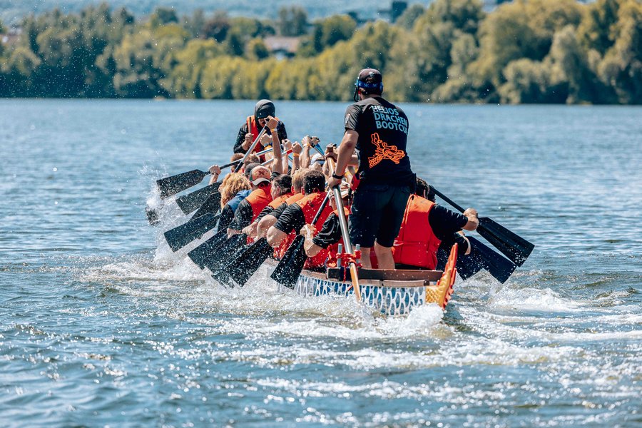 Eine Gruppe von Menschen paddelt gemeinsam in einem Drachenboot auf einem See.