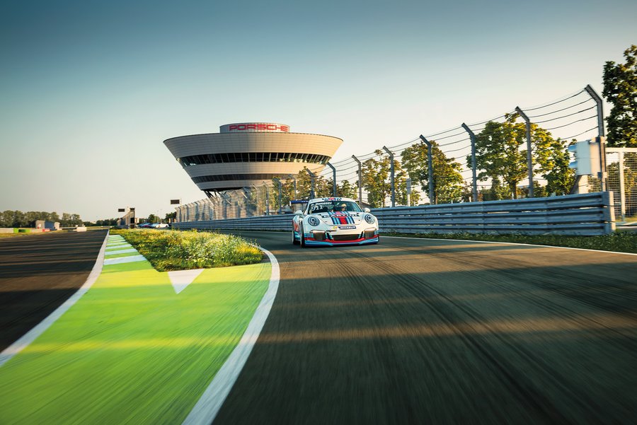 Ein Auto fährt auf einer Rennstrecke, im Hintergrund ist ein Gebäude sichtbar.