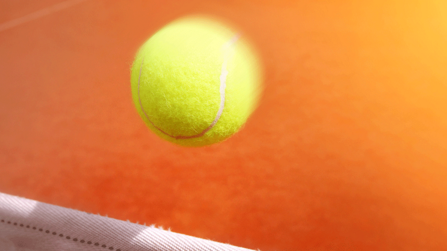 Eine Nahaufnahme eines leuchtend gelben Tennisballs, der in der Luft über einem Netz auf einem sonnenbeschienenen Tennisplatz fliegt. Der Hintergrund ist ein Farbverlauf in Orangetöne. Der Fokus liegt auf dem Ball, wobei das Netz und die Spielfeldlinien leicht unscharf sind.