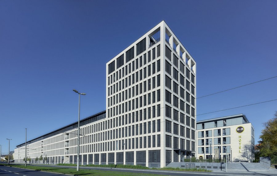 Ein modernes, mehrstöckiges Gebäude mit einer gitterartigen Fassade und großen Fenstern, gelegen neben einer Straße und einem grünen Rasen.